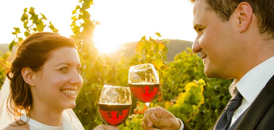 Brautpaar bei Sonnenuntergang mit Weinglass in den Weinbergen der Pfalz